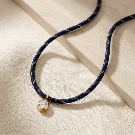 Navy rope necklace with gold-colored accents and a round clear pendant on ivory linen, AI-styled image.